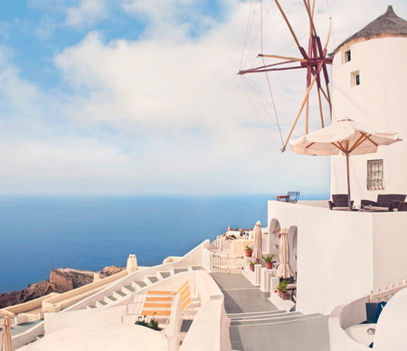 famous windmill with tables, umbrellas and sunbeds around it on sunny summer day on Santorini or Thira, Greeceの写真素材