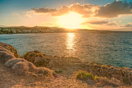 view of setting sun and city from cliff on small rocky island, Crete, Greeceの写真素材