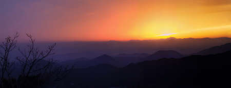 view of sunset over mountain range with branches at foreground in Palgongsan National Park in South Koreaの写真素材