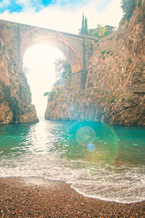 beautiful pebble beach overlooking old bridge at sunset with sun shining through at Fiordo di Furore, Amalfi coast, Italyの写真素材