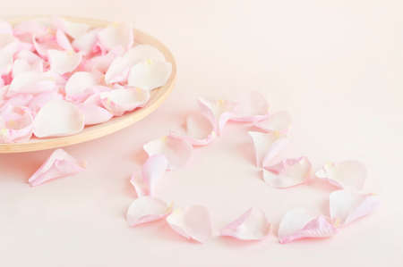 soft pink coloured image of rose petal heart and wooden plate filled with pink rose petalsの写真素材