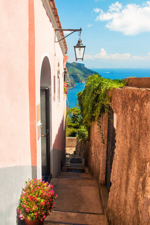 narrow street in mountain town with sea and mountains in background and flowers in foreground, Ravello, Amalfi, Italyの写真素材