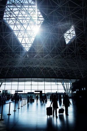two women in silhouette walking towards check-in desk in Zagreb airport hall, Croatia, on sunny day with sun shining through roof windowのeditorial素材