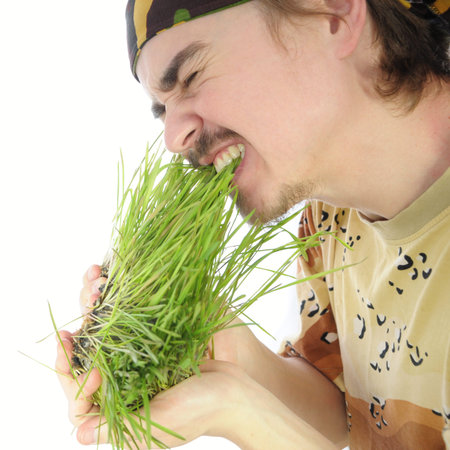 Young man biting and eating raw green grass