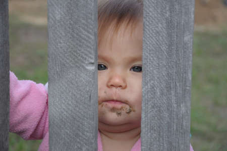 dirty rustic baby behind old wooden board looking through itの写真素材