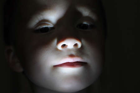 Little boy portrait in the dark lighted from the bottomの写真素材