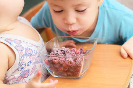 Boy blowing on frozen rasberries for heatingの写真素材