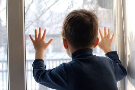 Boy  looking out the window with hands on the glassの写真素材