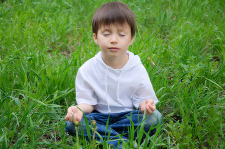 Caucasian cute boy sitting in meditation pose outside on the grassの写真素材
