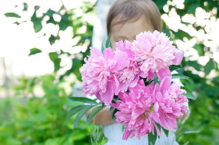 Little baby child  presenting a bouquet of peony flowersの写真素材