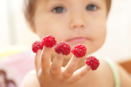 Little kid with raspberry on fingers, focus on handsの写真素材