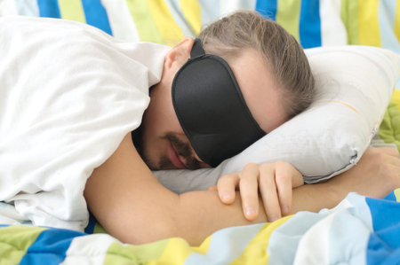 bearded young man sleeping with sleep mask in bed