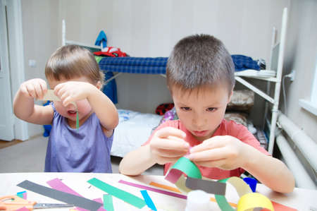 children development - kids making paper colored garland with glue on table, siblings craft, brother and sister playing togetherの写真素材