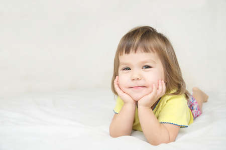 smiling happy little girl with cute cheeks lying on bed isolated, happy childhood conceptの写真素材