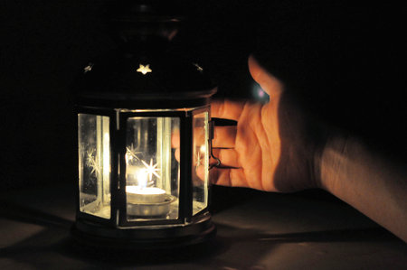 Hand illuminated wirt light from candle lantern in dark, black background with soft fire
