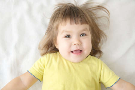 smiling happy little girl portrait expressive positive emotional face lying on bed isolated, happy childhood conceptの写真素材