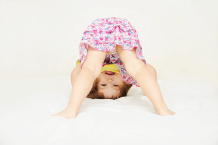Smiling little girl standing on head upside down isolated on white background