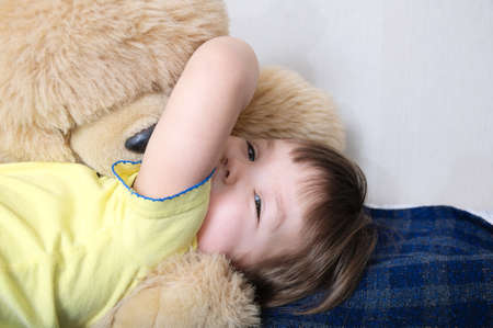 child playing with teddy bear toy indoor,happy childhood, smiling kid having fun lying on bedの写真素材