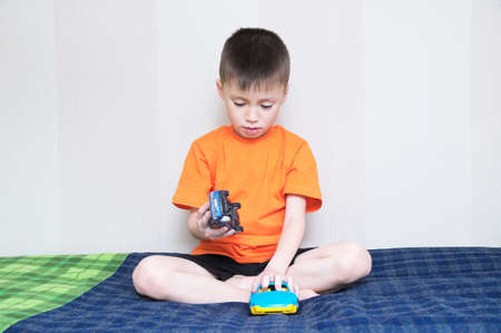 child playing car game,boy playing with toys sitting on bed indoor,kid holding two toy cars at home aloneの写真素材