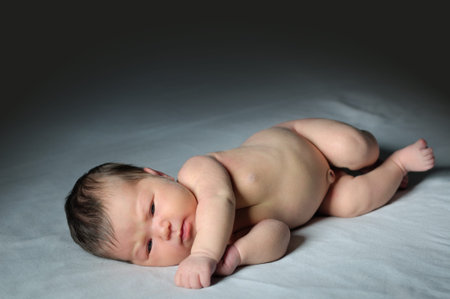 Newborn baby awaken on bed on dark background, asian baby full body portrait