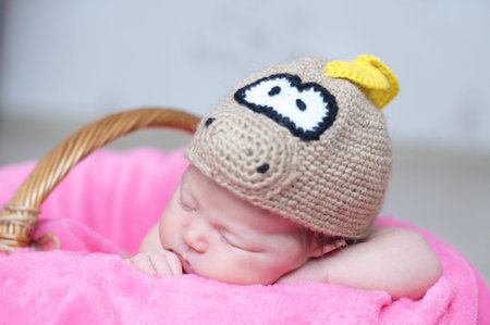 Cute happy newborn baby in dragon knitted cap sleeping in basket on pink blanket. Infant sleeping...
