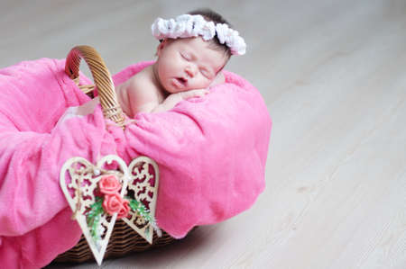decorated wooden hearts on basket on focus, newborn baby girl sleeping in basket, lying in pink blanket, cute child, daughter announcement cardの写真素材