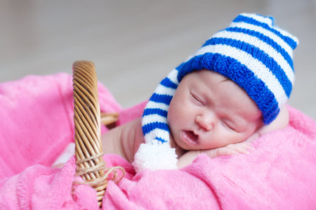 Cute happy newborn baby in striped knitted cap sleeping in basket on pink blanket. Infant sleeping portrait.の写真素材