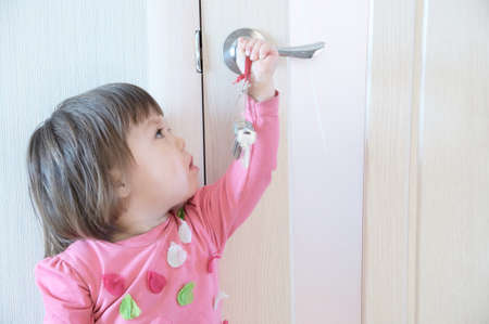 Child playing with keys forgotten by parents in door keyhole. Children safety and home safety concept.の写真素材