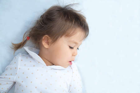 little girl portrait looking down with interest lying on white blanketの写真素材