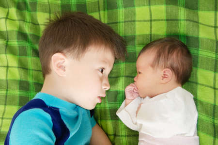 Brother and little newborn sister looking at each other lying facing on bedの写真素材