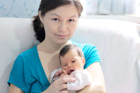 Asian smiling woman holding infant baby in her arms, happy motherhood conceptの写真素材
