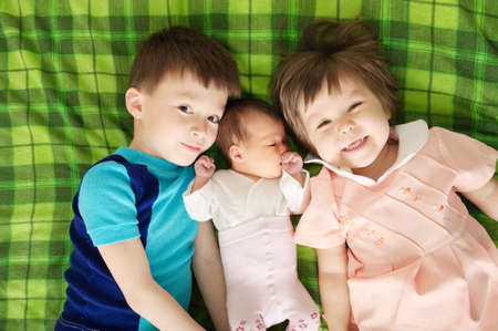 three sibling children lying on bed in large family, hug and embrace with loveの写真素材