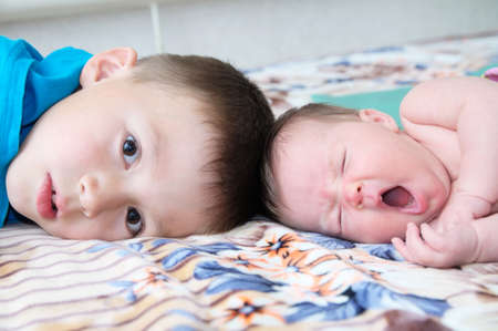 Brother and little newborn sister yawning lying on bed at home togetherの写真素材
