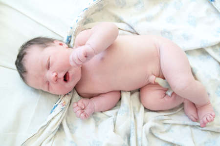 Infant baby with umbilical cord first day of life lying on drapery sheetsの写真素材