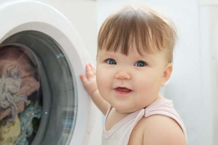Baby portrait near washing machine looking at camera,  having fun and playing with washerの写真素材