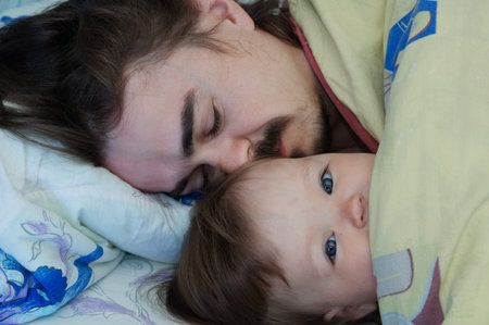 Little baby girl wake up in the morning. Parent tired sleeping. Father lying on bed. Happy family.