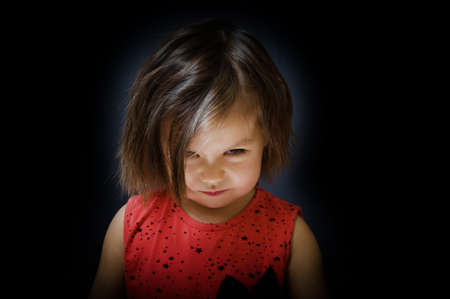 Tricky child look up and smiling sly on dark background. little girl deviousの写真素材