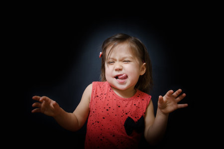 Child having fun and showing tongue on dark background. funny little girl dancing in the darkness