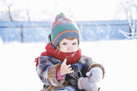 baby in winter clothes outdoor. cute child in cap,scarf and mittens among the snowの写真素材