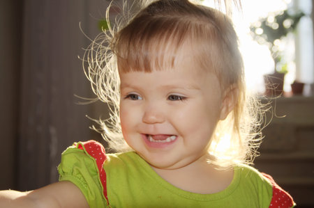 backlight portrait of baby girl smiling,tousled hair of happy talking child, sunset through window