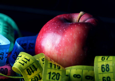 colored measuring tape and an apple on a black background