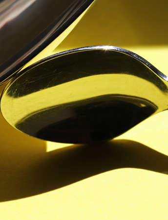 close-up metal spoon with shadows on yellow backgroundの写真素材
