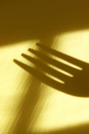 close-up metal fork with shadows on yellow backgroundの写真素材