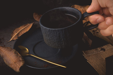Coffee cup and golden spoon on black background with autumn leaves