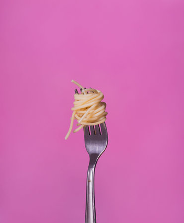 Silver fork with spaghetti on a pink background. Front view