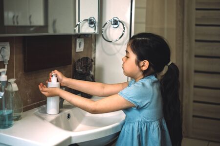 A child washes in blue dress his hands with sanitizer over a white sinkの写真素材