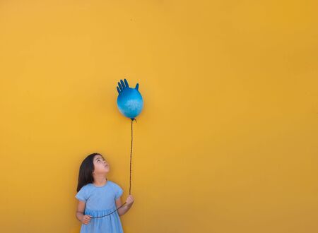 A sad girl holds an inflated glove in her hand instead of a balloon, it is her birthday during the coronovirus pandemic. Bannerの写真素材