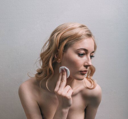 A girl with open shoulders touches her face with a cotton padの写真素材