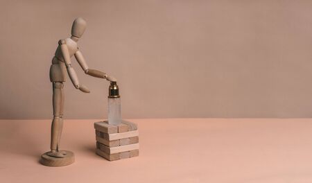 A wooden man uses a disinfectant standing on wooden parts on a beige backgroundの写真素材