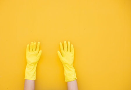 Hands in yellow rubber gloves on a yellow backgroundの写真素材